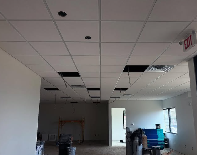 Interior view of a room with a suspended ceiling, unfinished, with holes for lights and vents. 