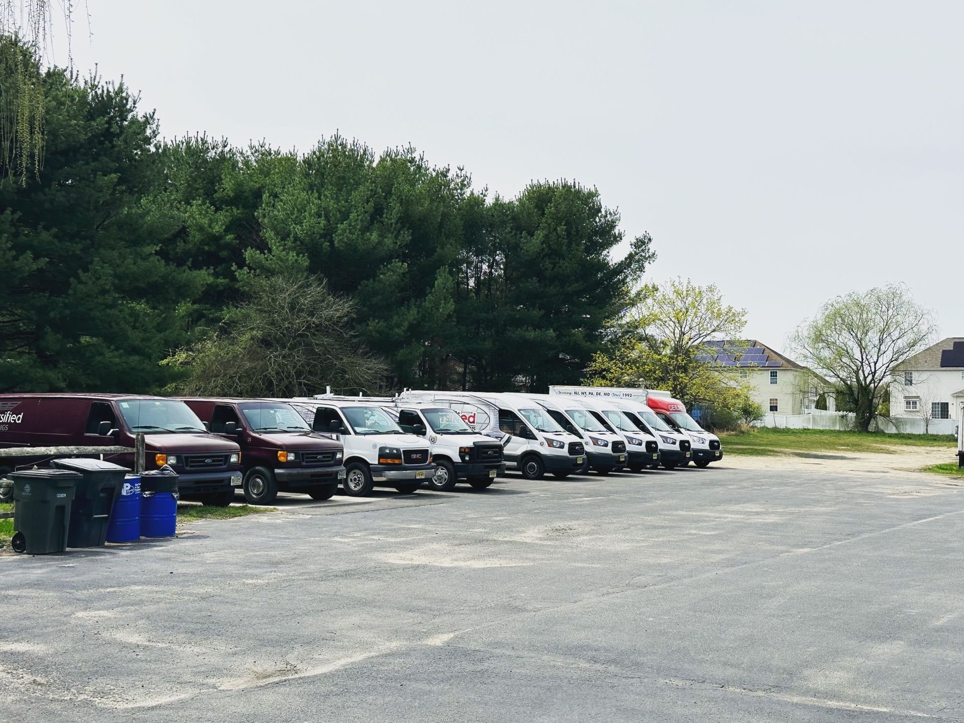 Vehicles parked in a gravel lot with a treeline and a building in the background.