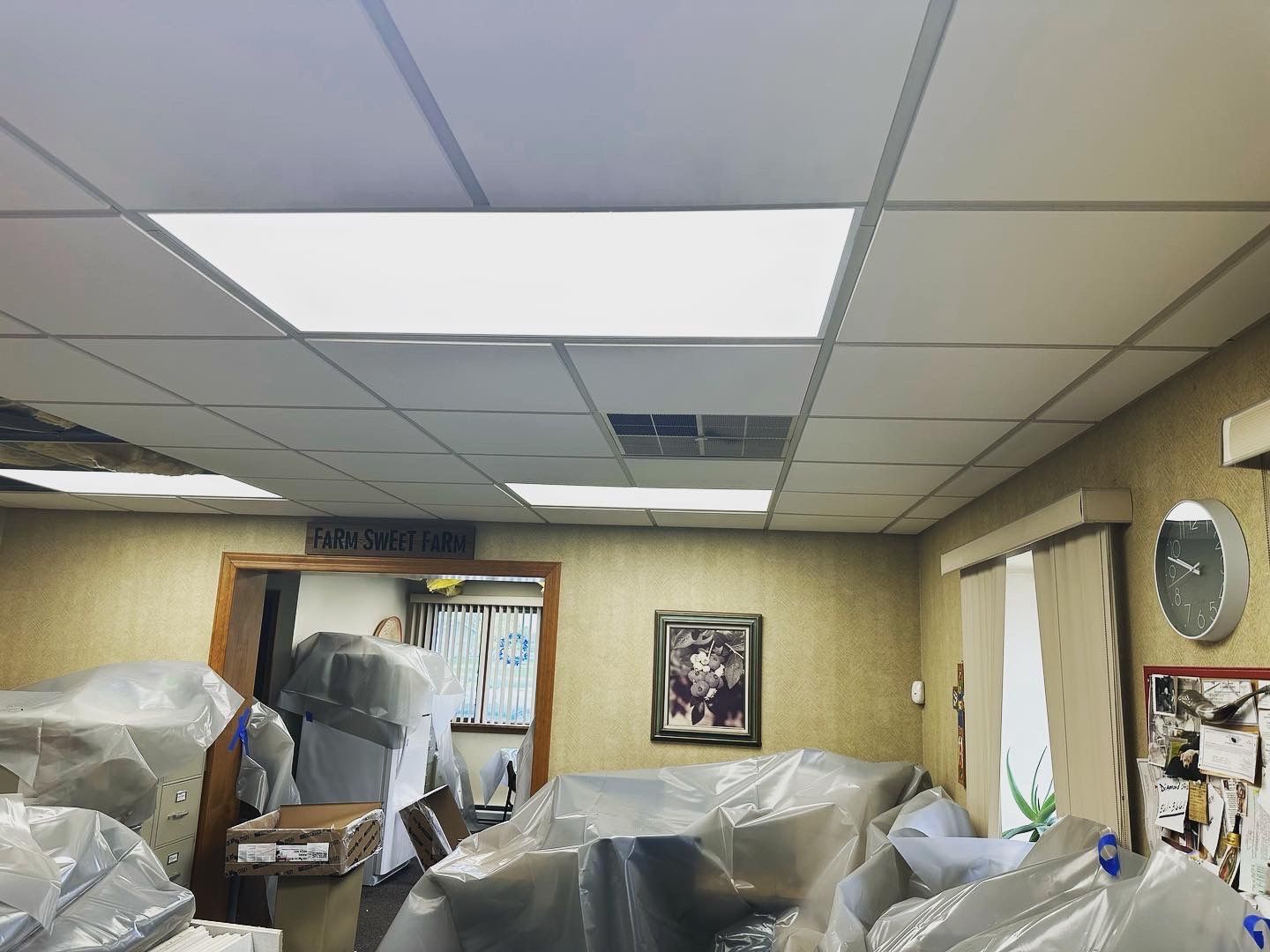 Office ceiling with fluorescent lights and covered furniture; doorway visible.