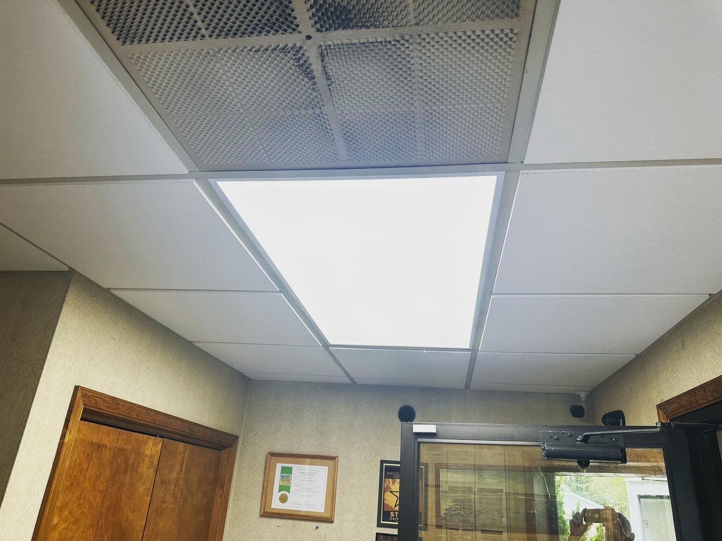 White ceiling tiles with overhead lighting; partially visible doorframe and wall.