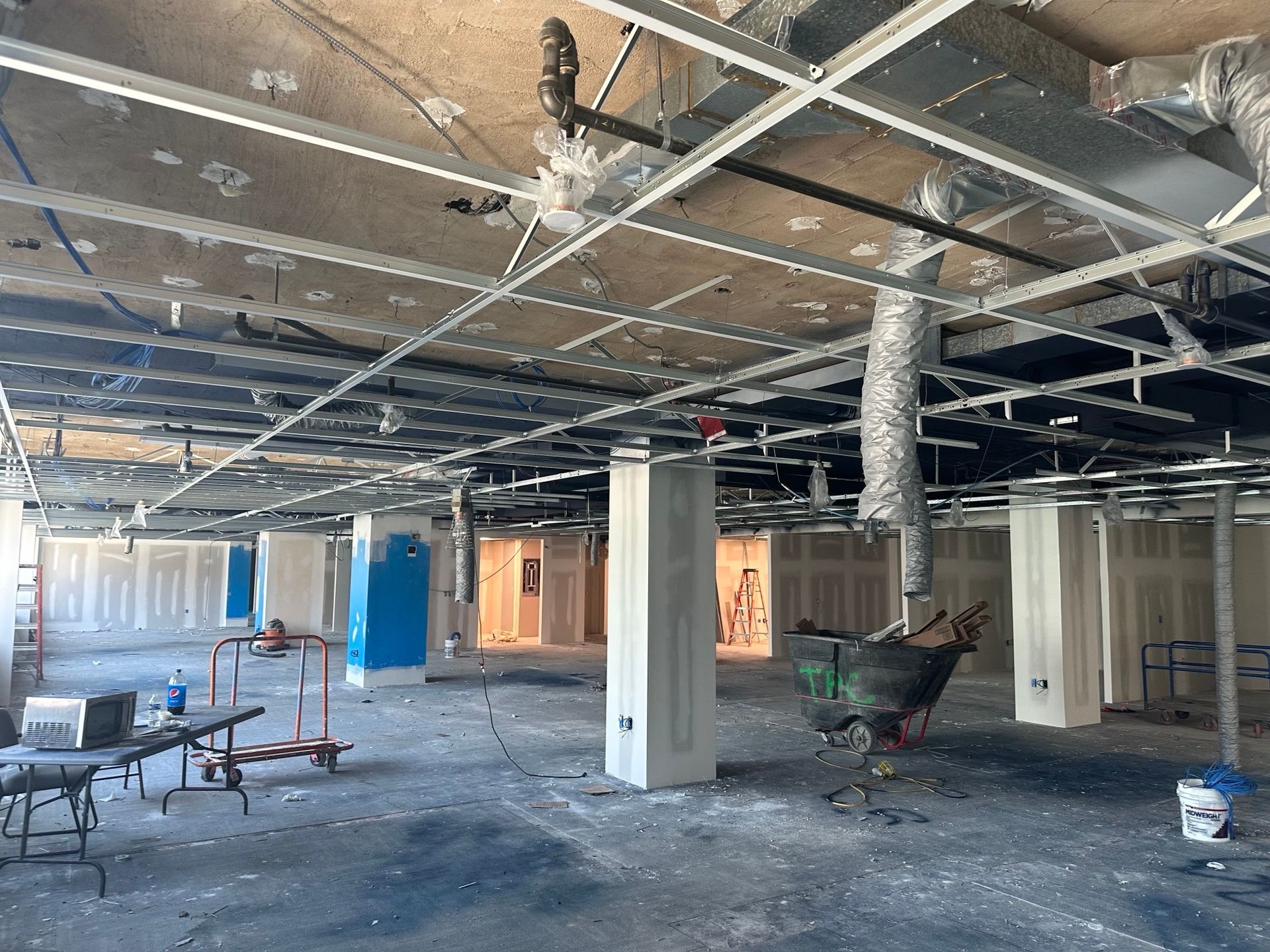 Construction site interior with exposed ceiling grid, ductwork, columns, and partially constructed walls.