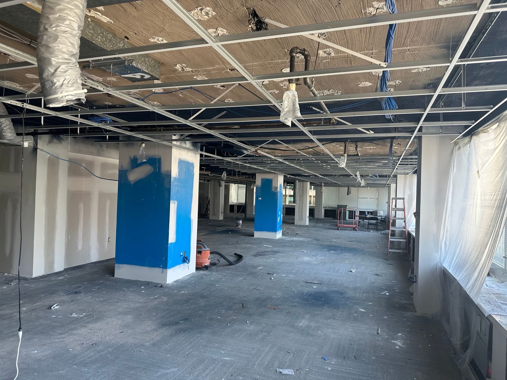 Interior view of a construction site. Ceiling infrastructure exposed, blue support beams.