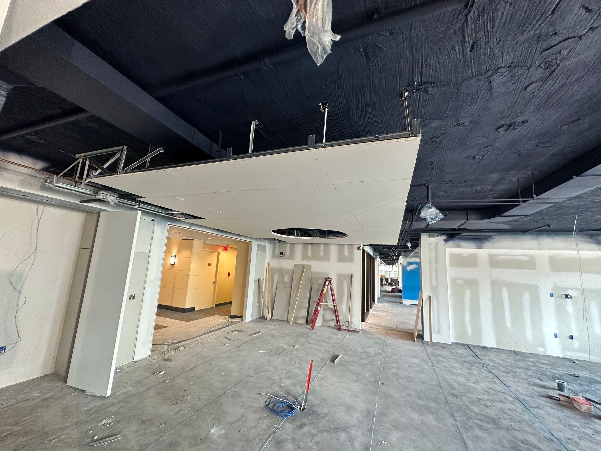 Interior construction site with exposed ceiling, drywall, and scattered tools.