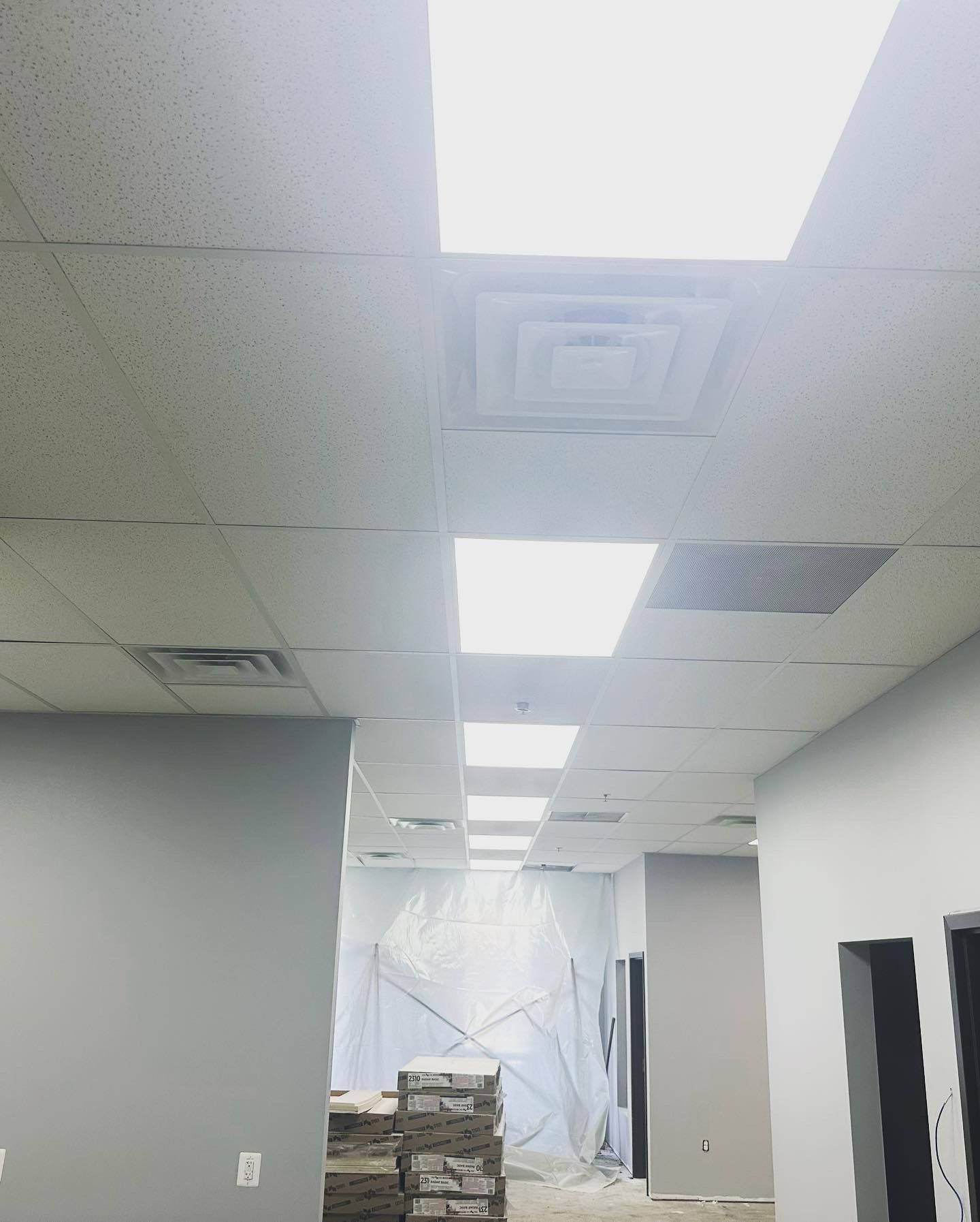 Interior view of a hallway with fluorescent ceiling lights and air vents. Gray walls and a neutral-toned ceiling.