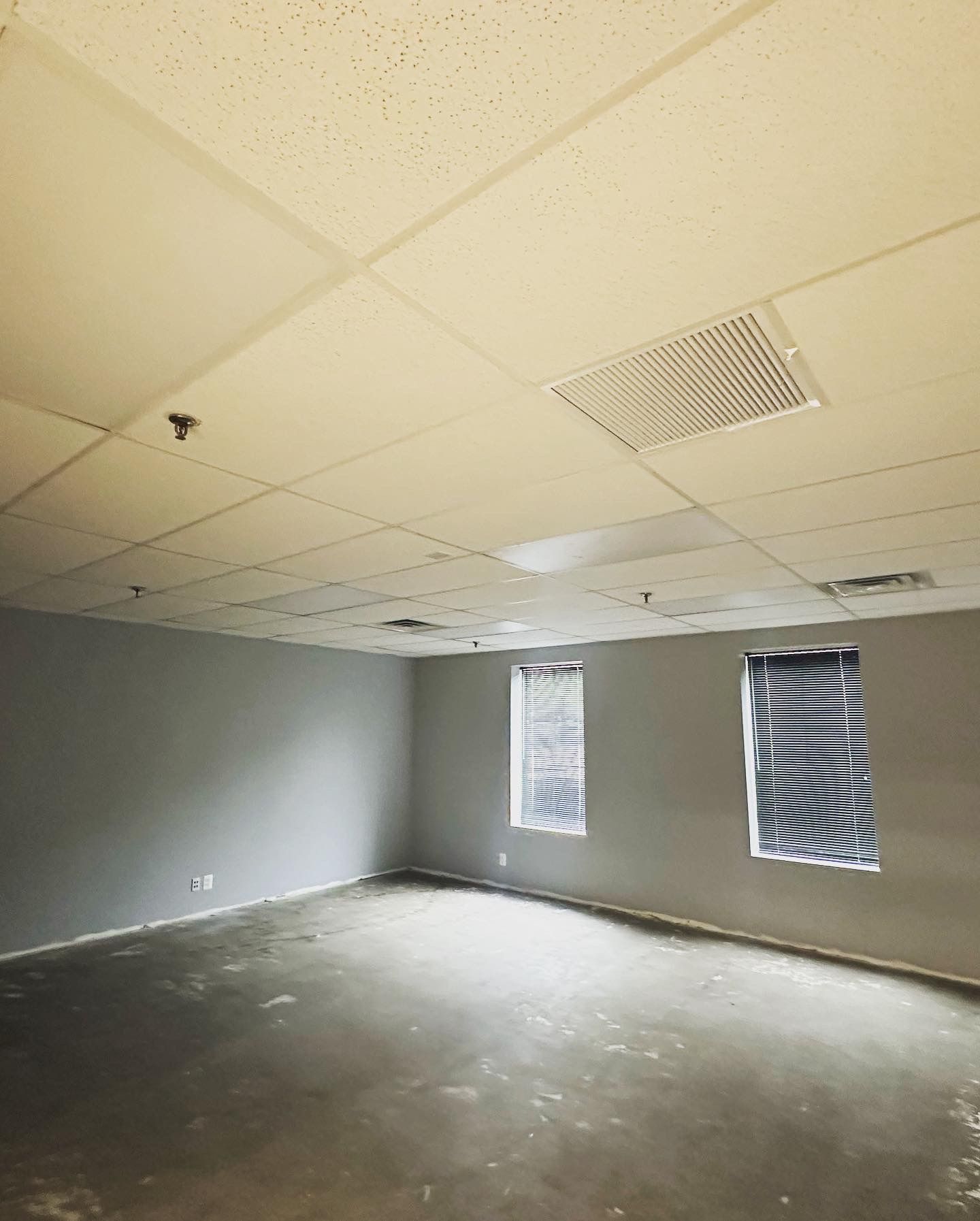 Empty room with gray walls, tiled ceiling, and three windows covered.