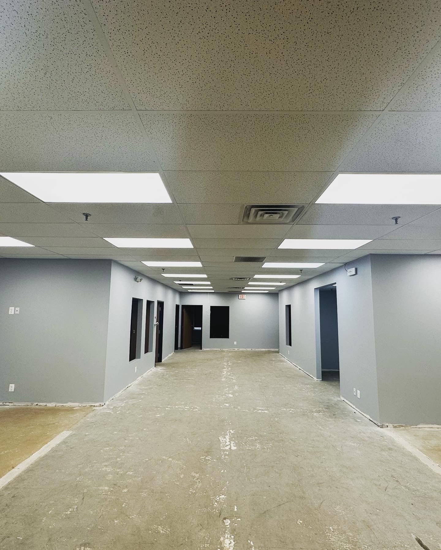 Long hallway with gray walls, multiple doorways, and drop ceiling with recessed lighting.