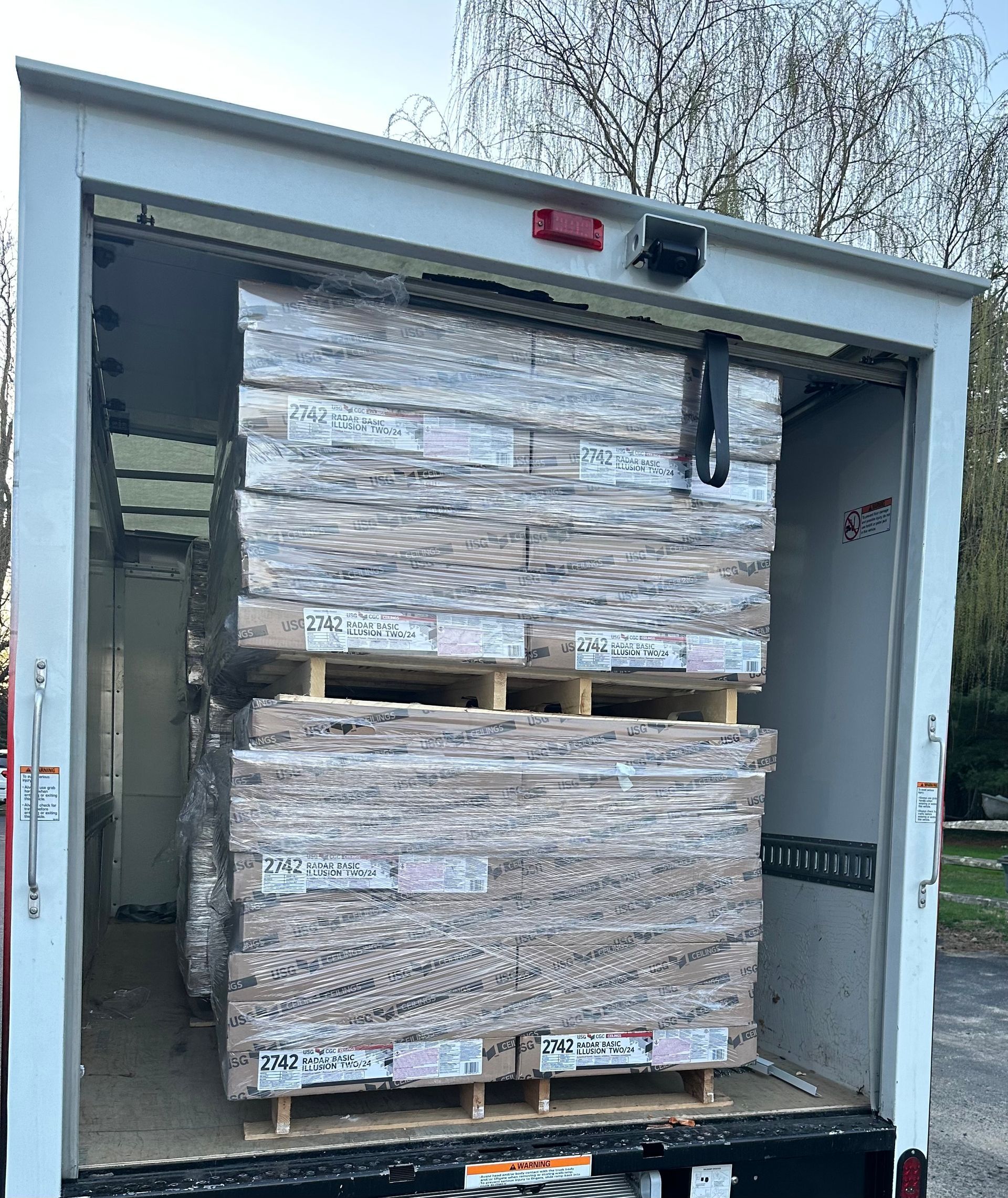 Open cargo truck loaded with two stacked pallets of wrapped rectangular items.