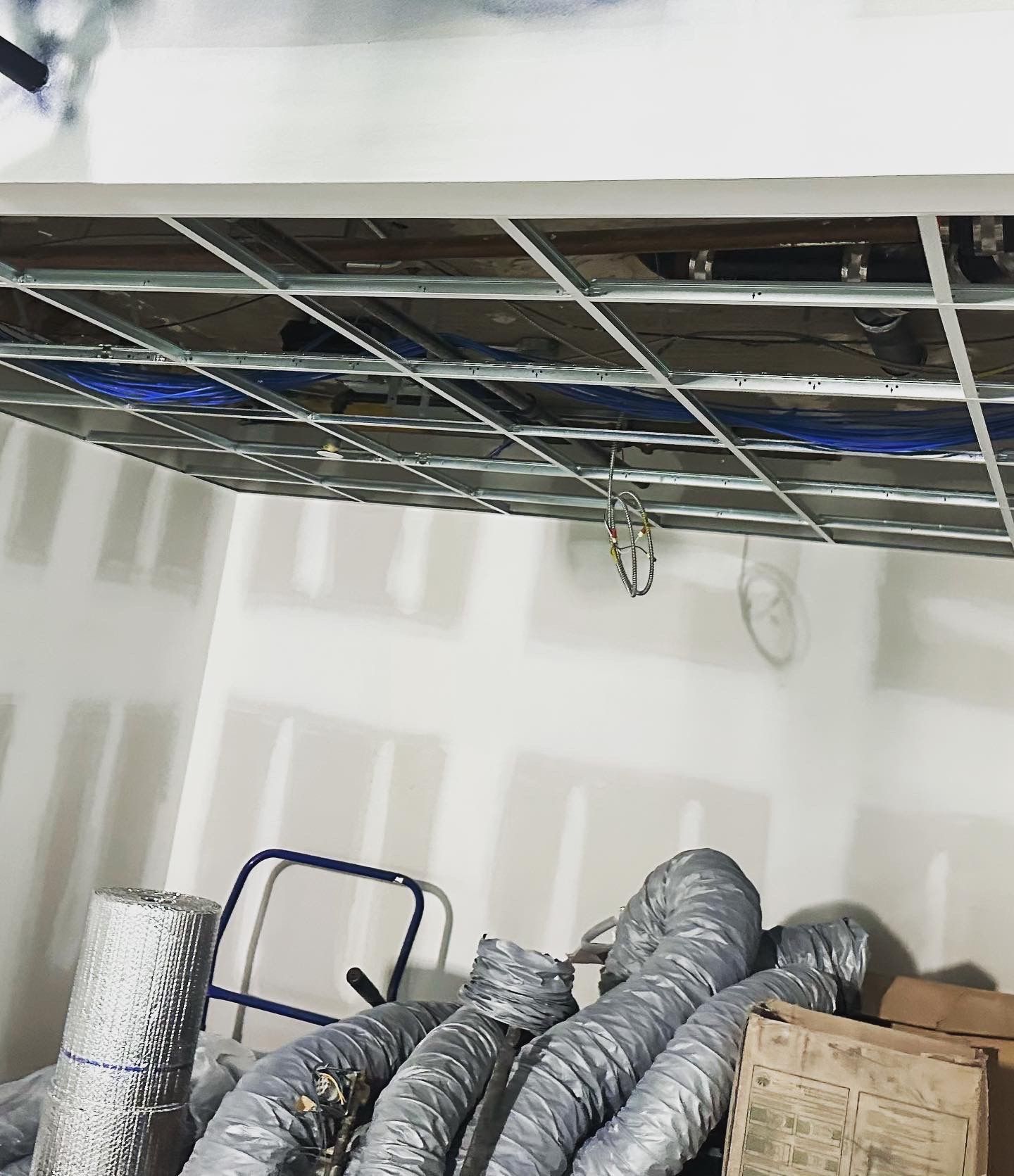 Construction site interior with exposed ceiling grid, air ducts, and materials on the floor.