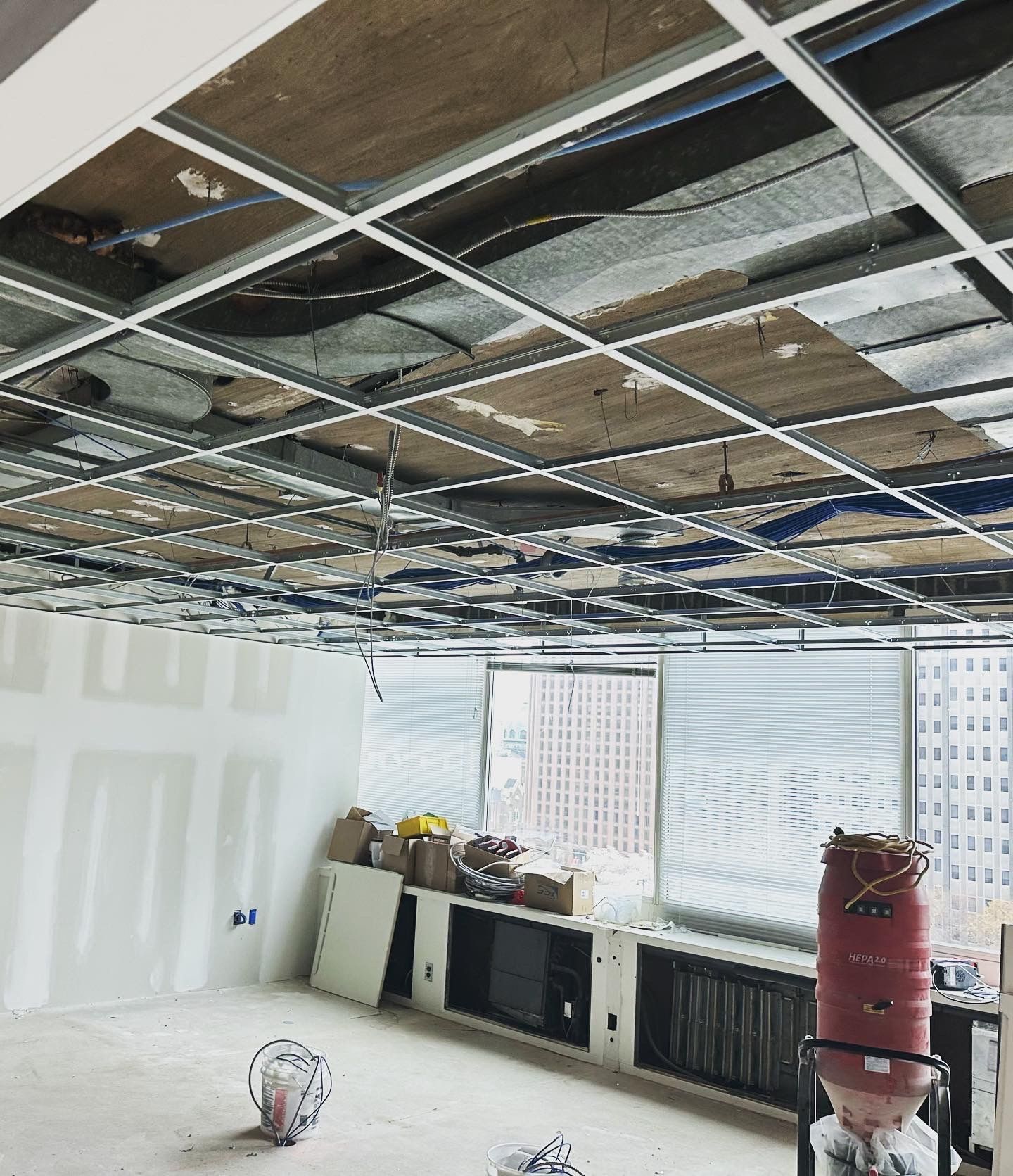 Office space under construction with exposed ceiling grid, drywall, and a red fire extinguisher.