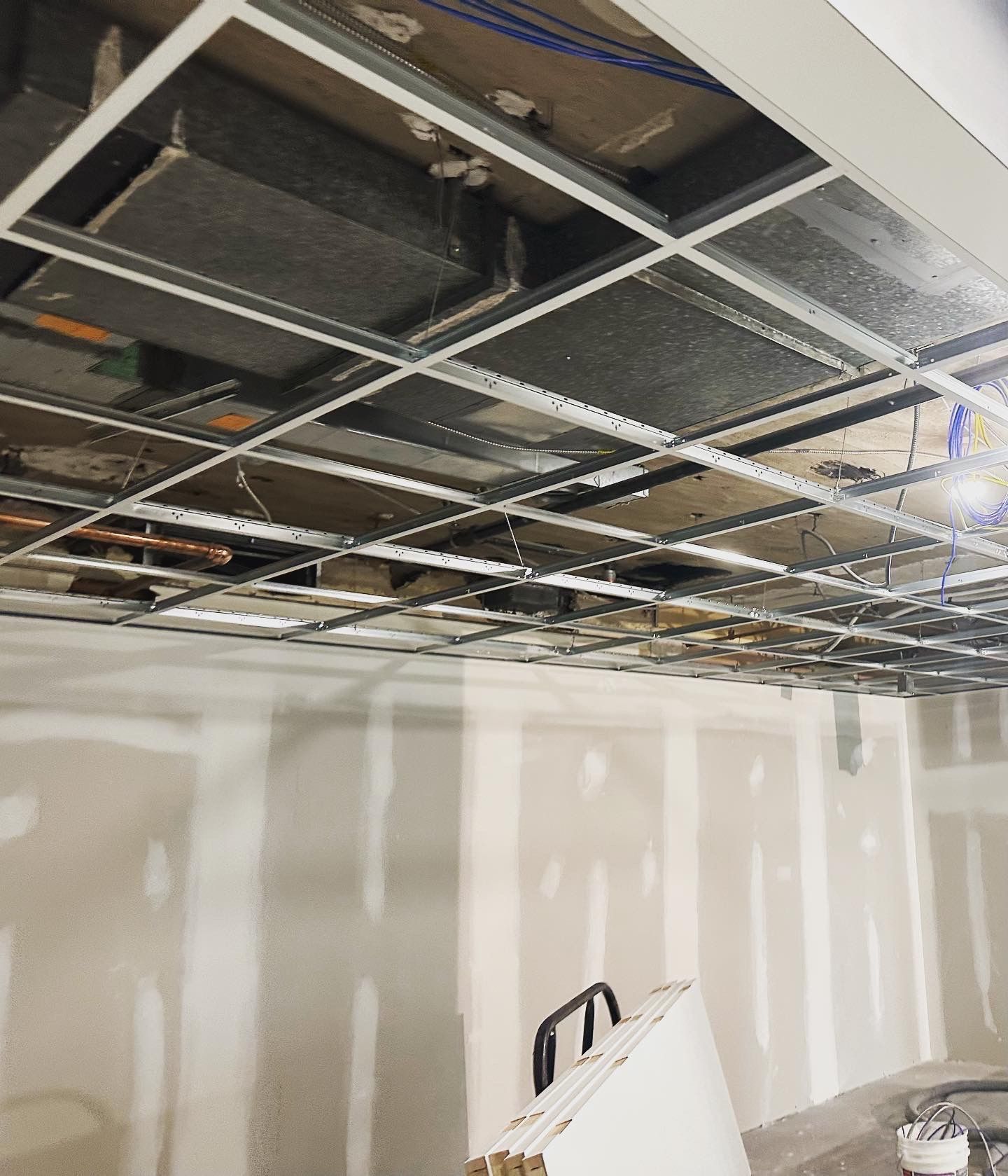 Construction site ceiling with exposed grid, wires, and drywall.