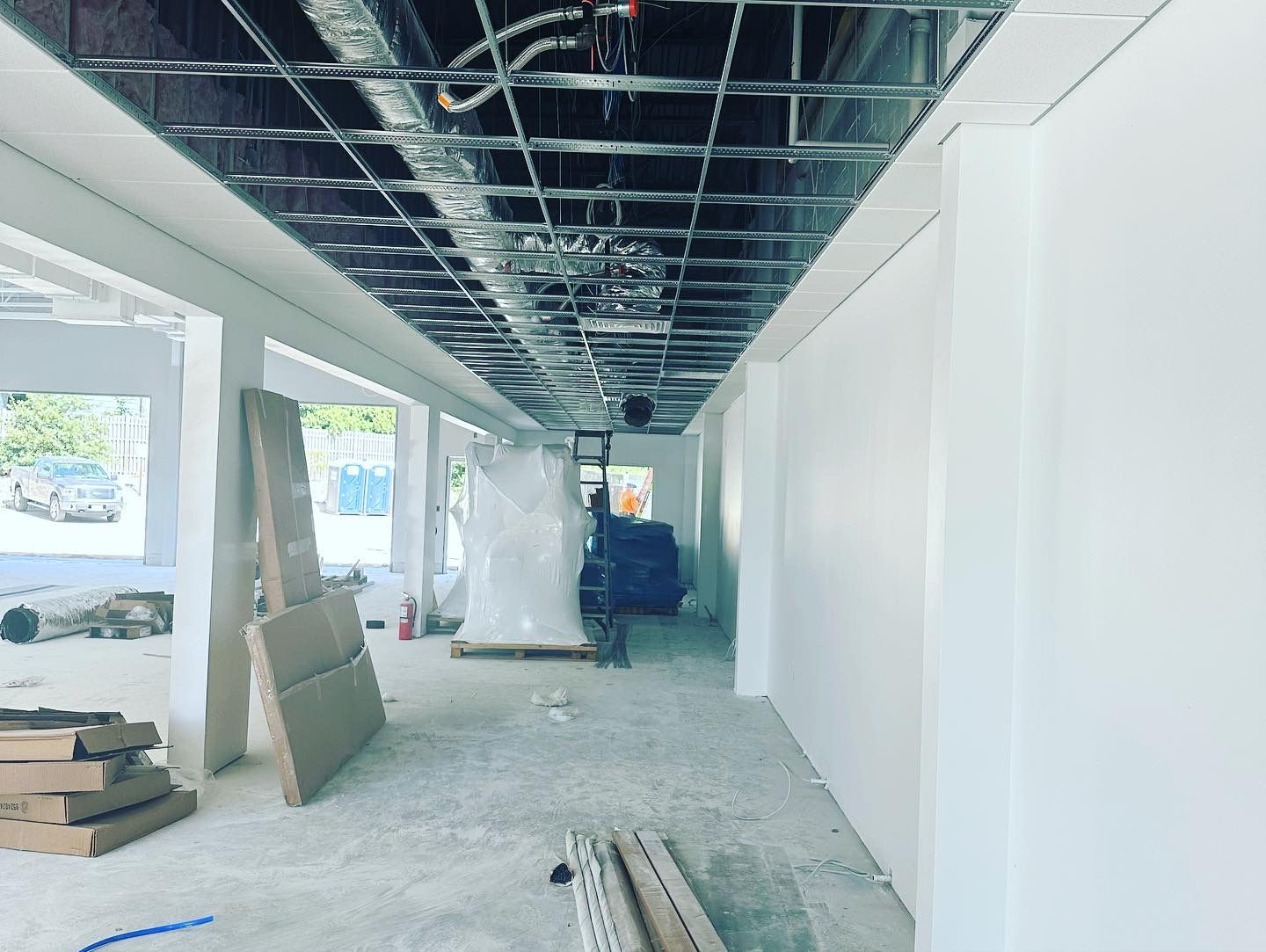Interior of a building under construction. White walls, a metal grid ceiling, and construction materials are visible.