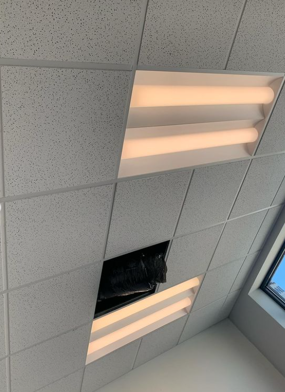 Ceiling tiles with recessed lighting, one tile missing revealing a dark void.