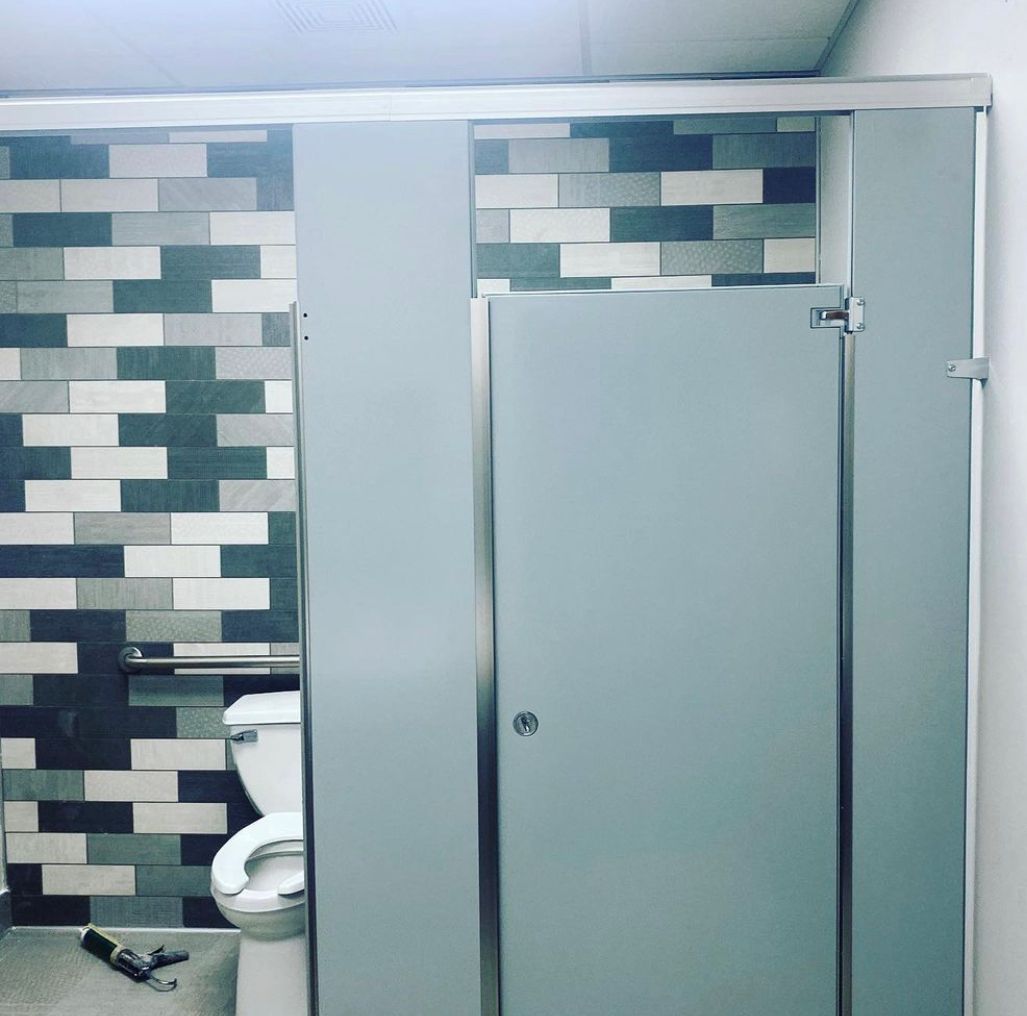 Bathroom with gray stall doors, toilet, and a brick-patterned tile wall.