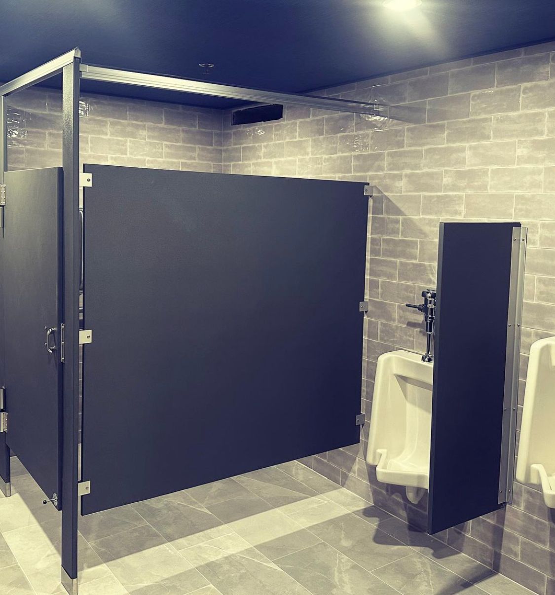 Public restroom with gray brick walls, urinals, and a black stall.