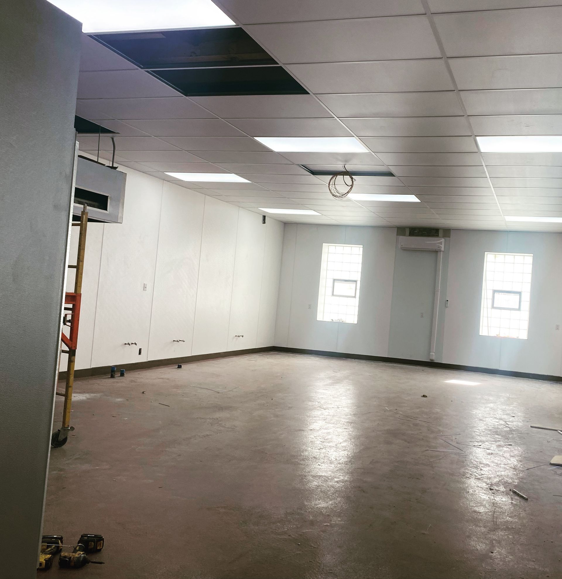 Empty room with white walls, ceiling, and windows; concrete floor.