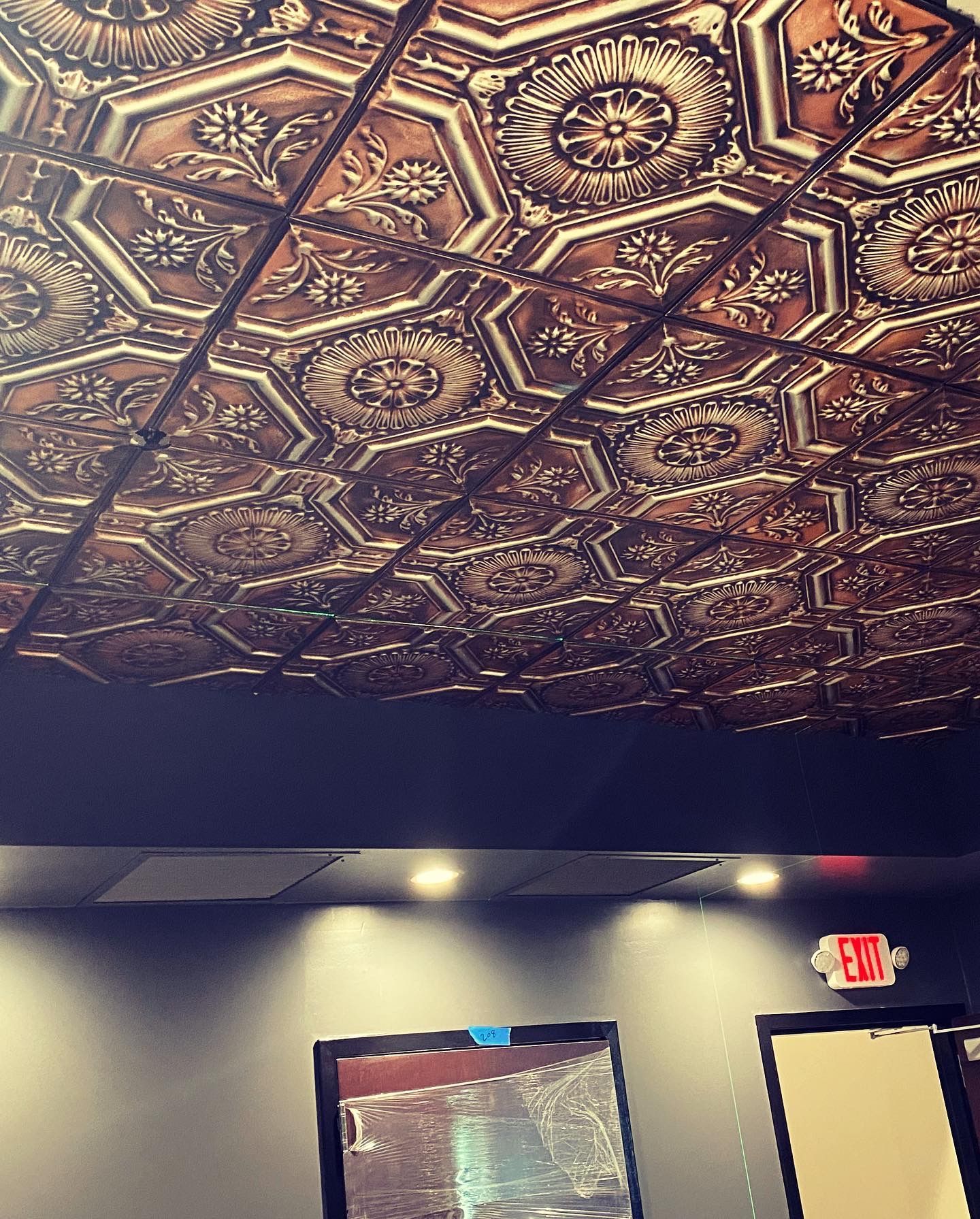 Ornate copper-colored ceiling tiles with a dark wall and recessed lighting.