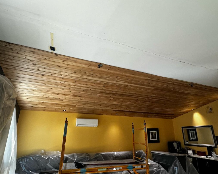 Interior room with yellow walls, wood plank ceiling, and furniture covered in plastic.
