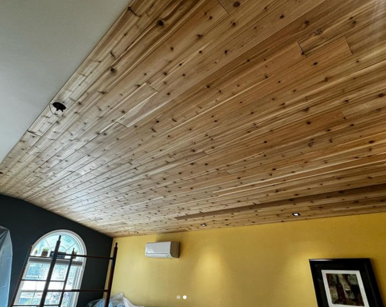 Wood-plank ceiling in a room with yellow and dark gray walls, and an arched window.