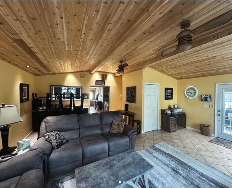Living room with wood-paneled ceiling, yellow walls, gray sofa, and tiled floor.