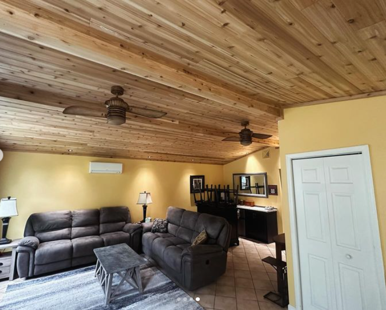 Living room with wood-paneled ceiling, two ceiling fans, brown recliners, and yellow walls.