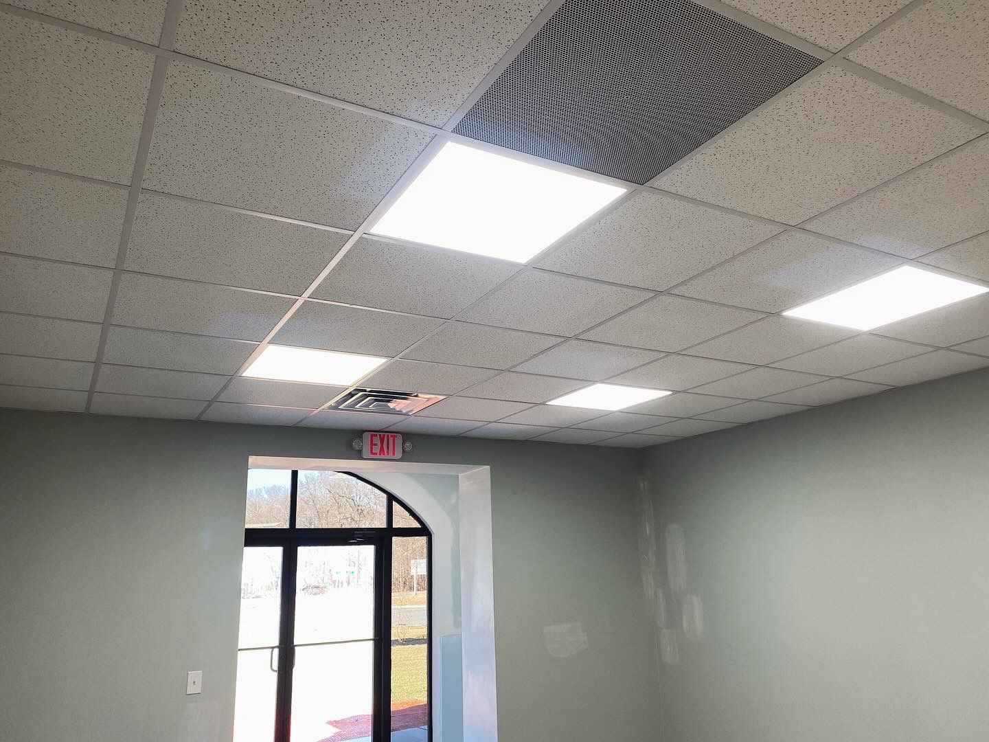 A drop-tile ceiling with recessed lights, exit sign, and a doorway with outdoor view.