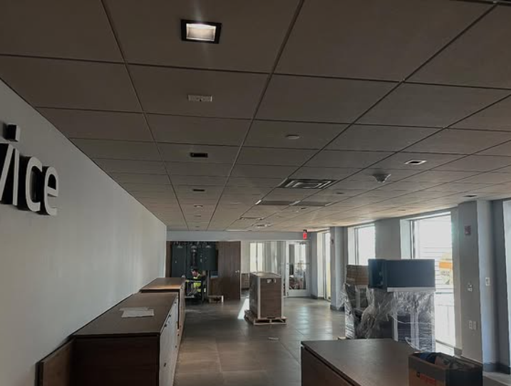 Empty office hallway with wood-tone furniture, ceiling tiles, and large windows with natural light.