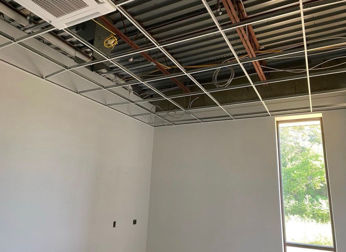 Room under construction with exposed ceiling grid, wires, and a window.