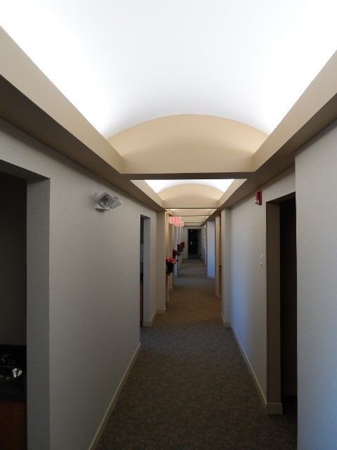 Long hallway with beige walls, doors, and a curved ceiling. Carpeted floor.