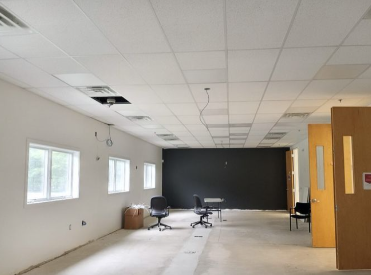 An empty office space with white walls, windows, and black accent wall, with chairs and tables present.