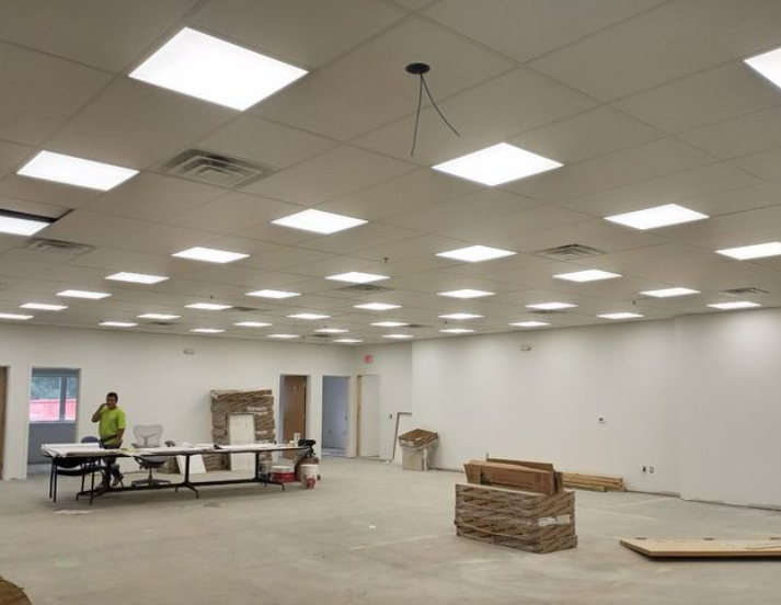 Interior view of a large room under construction with bright ceiling lights and a worker at a table.