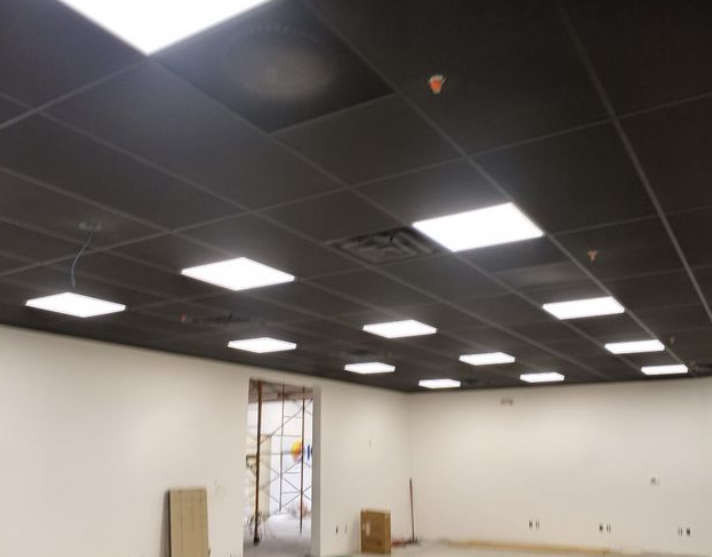 Black ceiling with square inset lights in an empty room with white walls, unfinished doorway, and boxes.