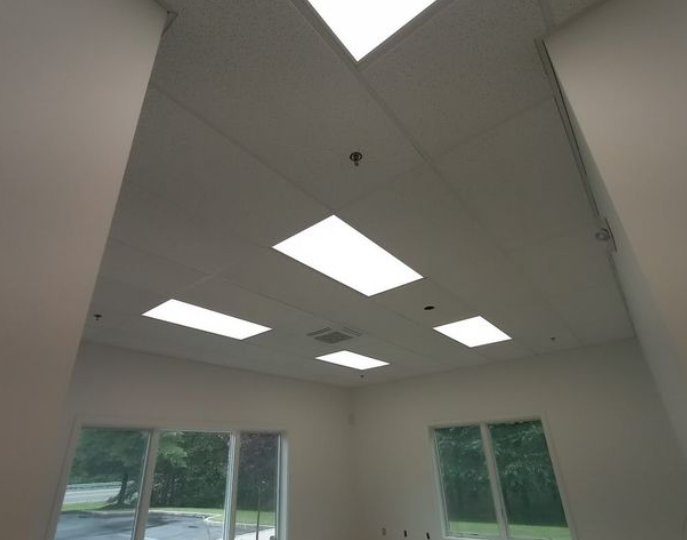 White ceiling with recessed rectangular lights in a room with windows and white walls.