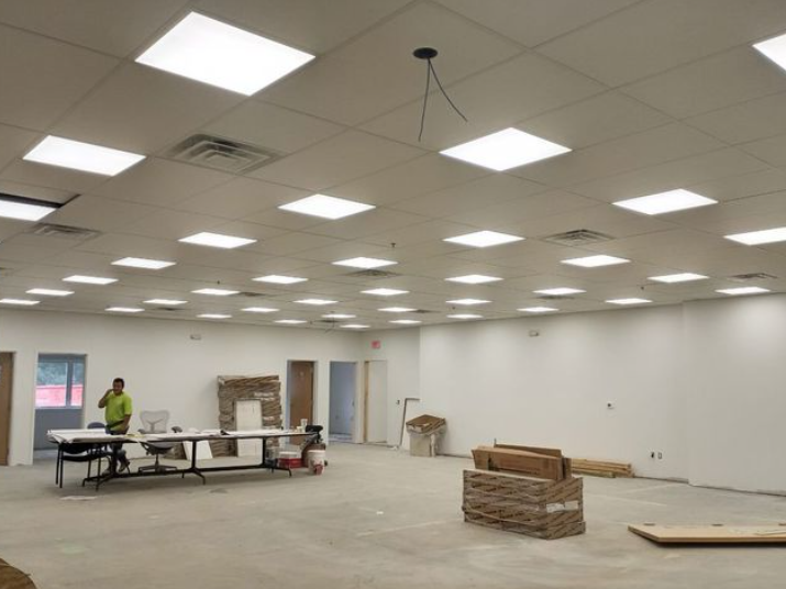 Large, empty room with bright ceiling lights; a person stands near a table, construction materials present.