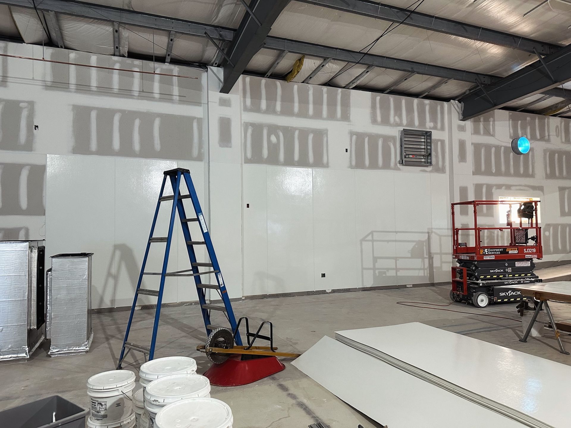 Interior of a building under construction. Walls are partially covered with white panels and drywall. 