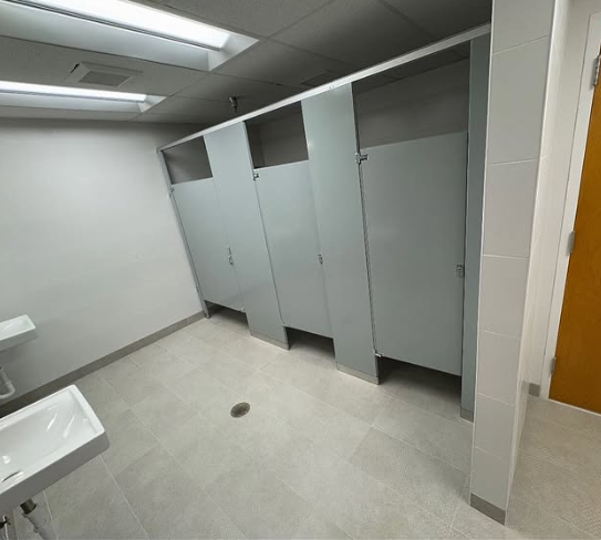 Empty public restroom with gray stalls, white sinks, and light gray tile flooring.