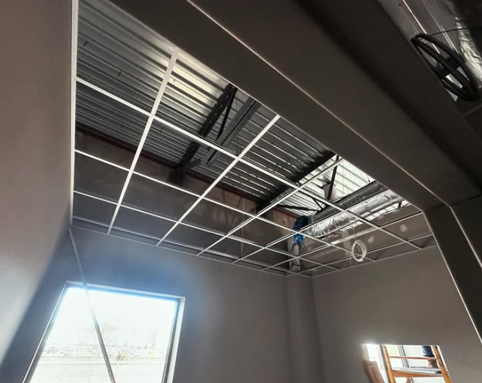 Interior of a room under construction, with a metal ceiling grid and unfinished walls.