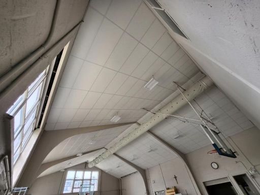 High angle view of a gymnasium ceiling with windows, lights, and a basketball hoop.