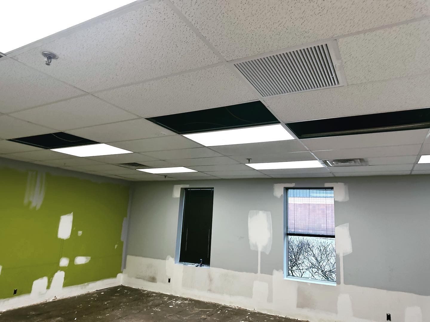 Interior room under construction, with exposed ceiling tiles and unfinished walls in green and gray.