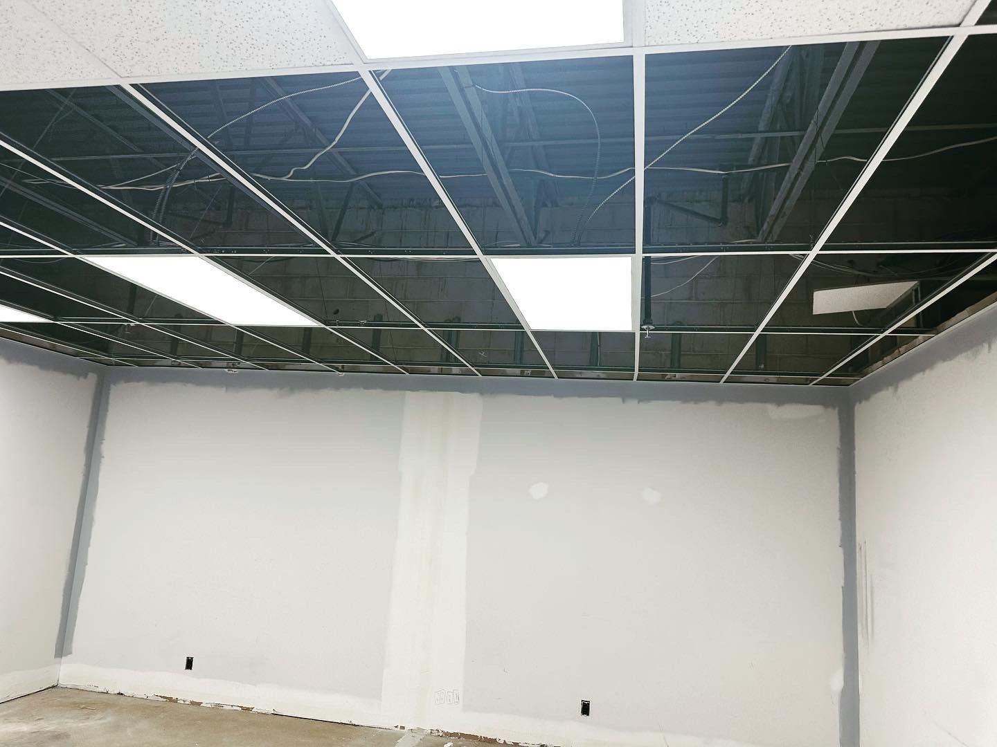 Room under construction, exposed ceiling grid, drywall walls, and unfinished ceiling tiles.