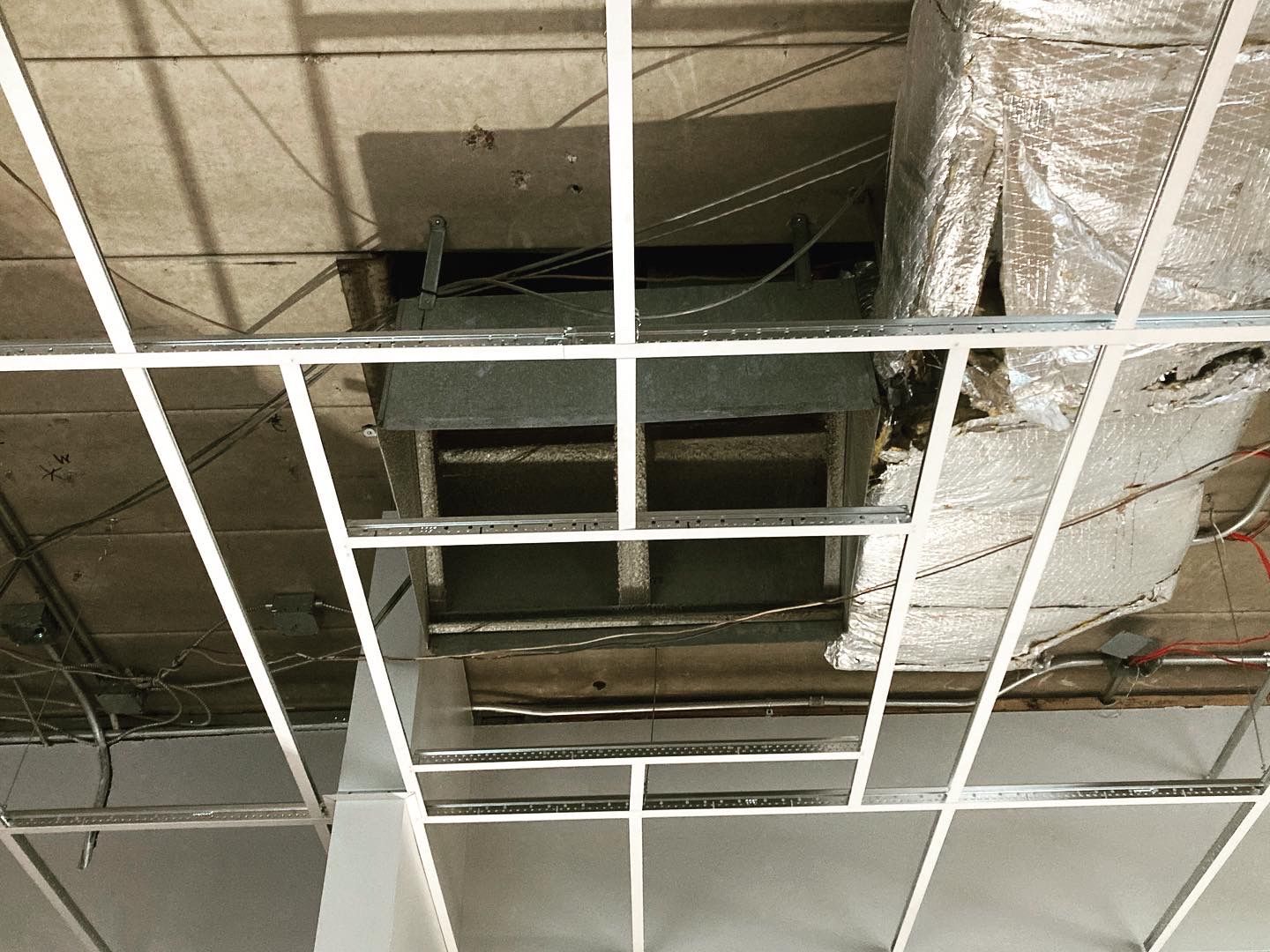 Ceiling grid with exposed HVAC ductwork and wires.