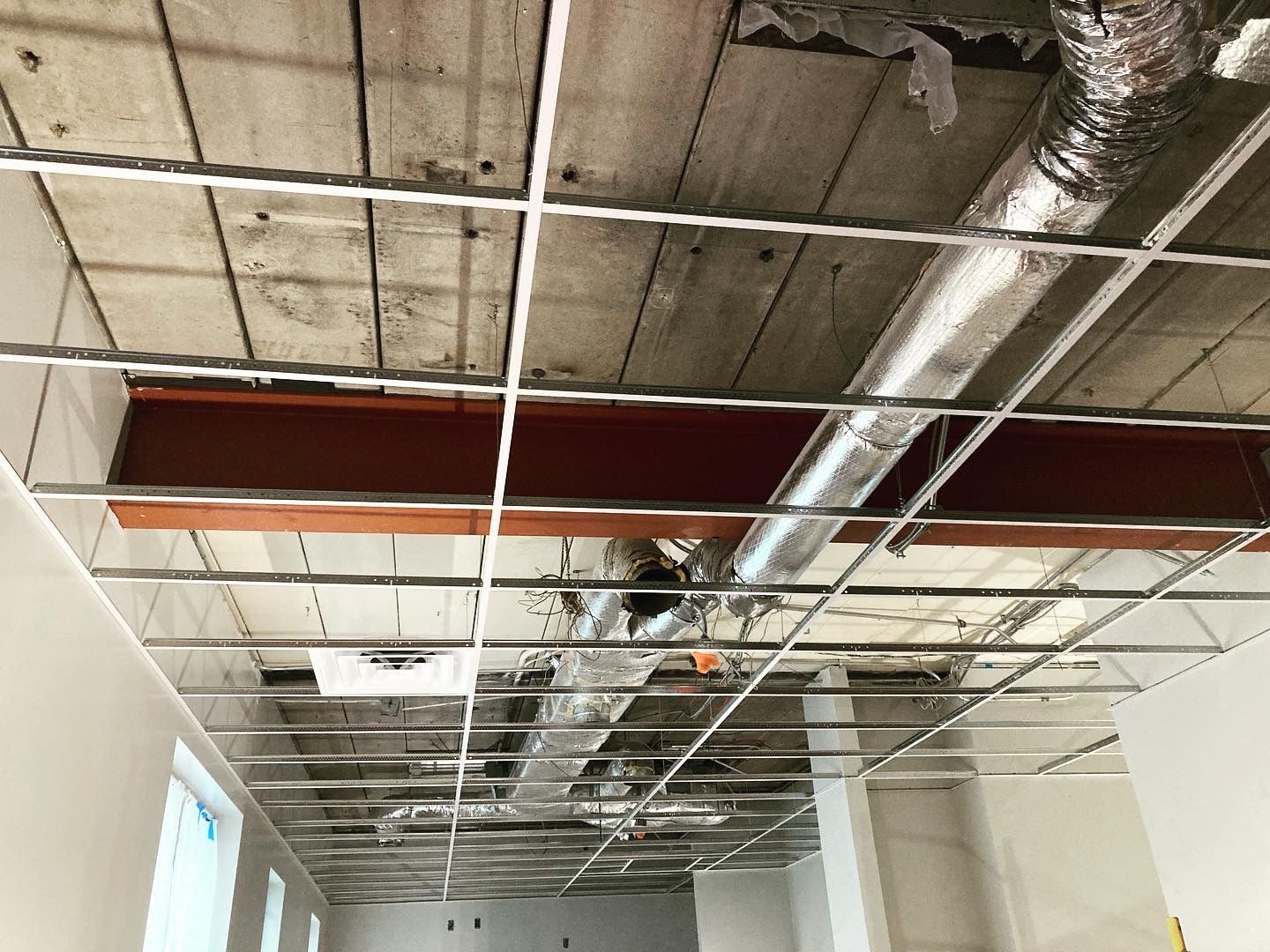 Construction site ceiling showing metal grid, ductwork, and a steel beam.