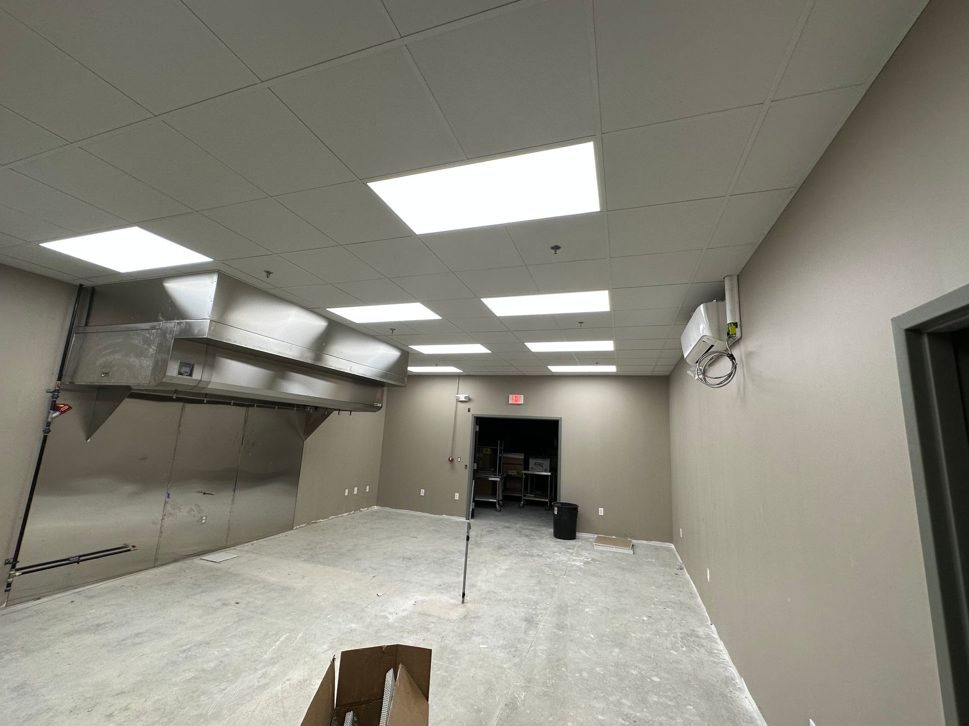 Empty, light-filled room with gray walls, white ceiling lights, and a stainless steel range hood.
