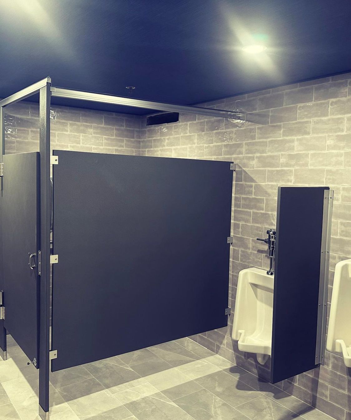 Bathroom with stalls and urinals. Gray brick wall and dark-colored stall doors.