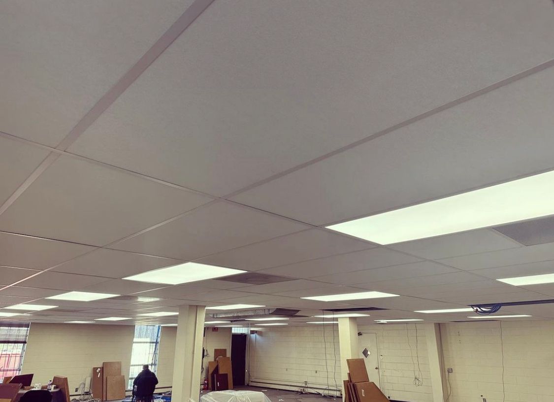 White ceiling with recessed fluorescent lights. Person in dark clothing in the background of an empty room.