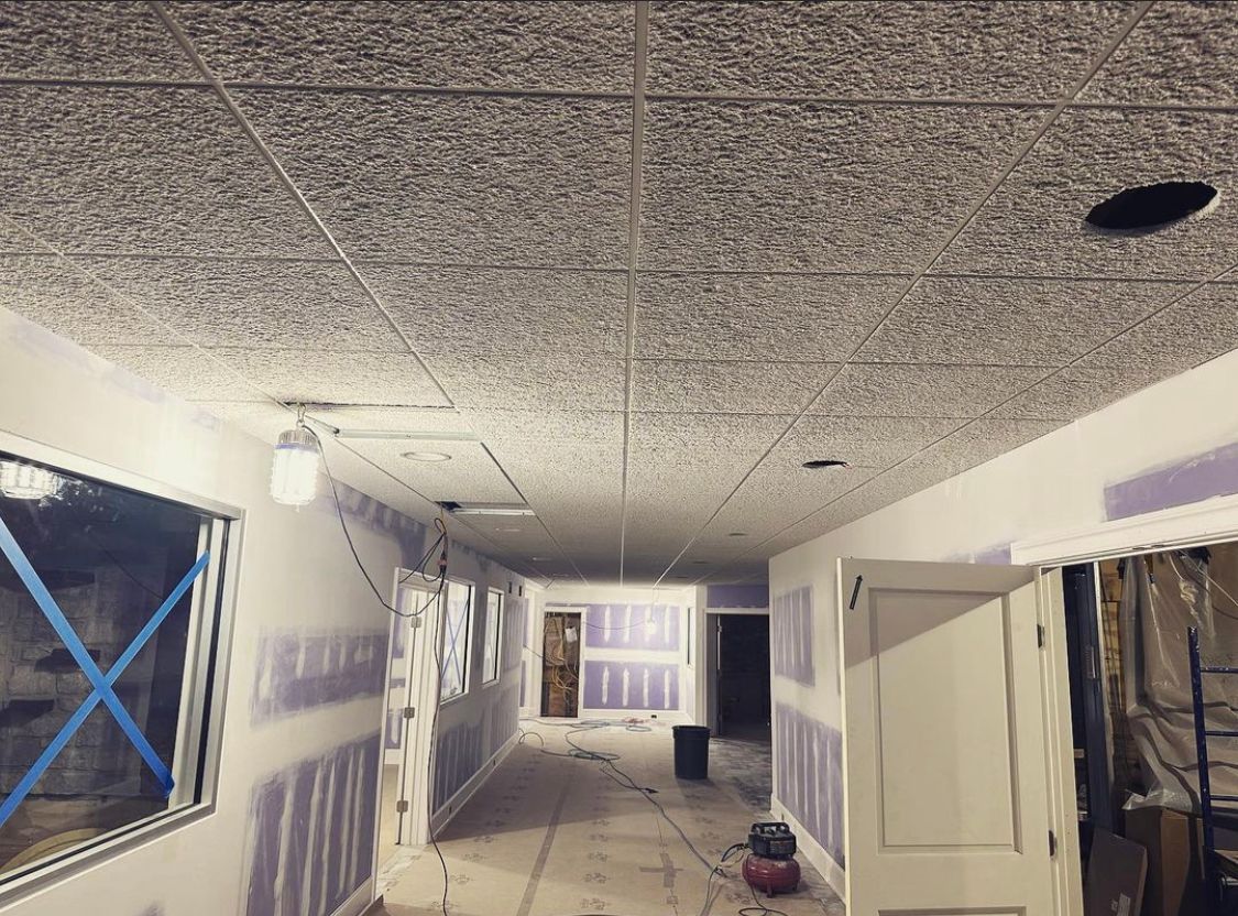 Interior view of a hallway under construction; exposed drywall, unfinished ceiling with recessed lights, and a window.