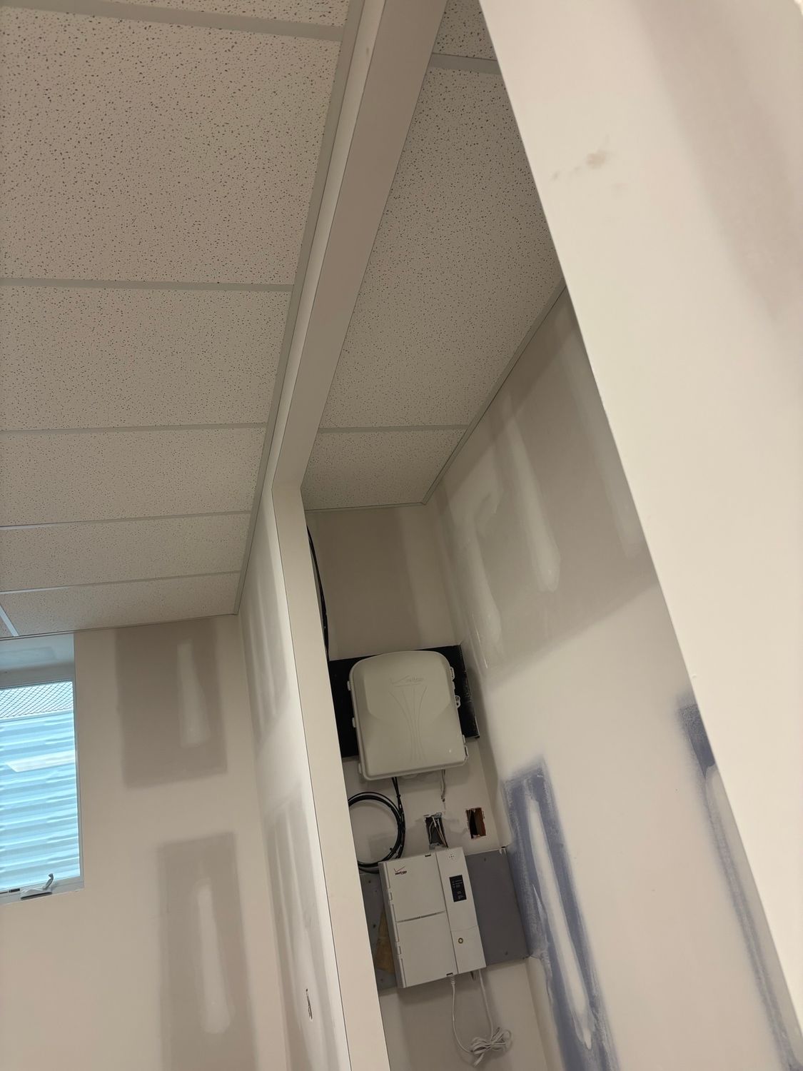 Room with white walls and ceiling tiles. Electrical panel on wall.
