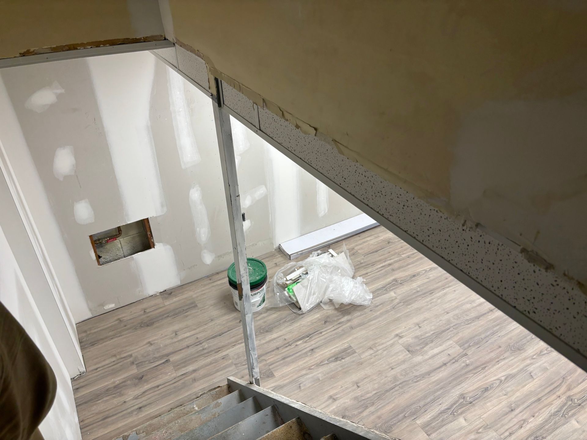 Stairwell under construction; drywall, flooring, and metal studs visible. Bucket and debris on the floor.