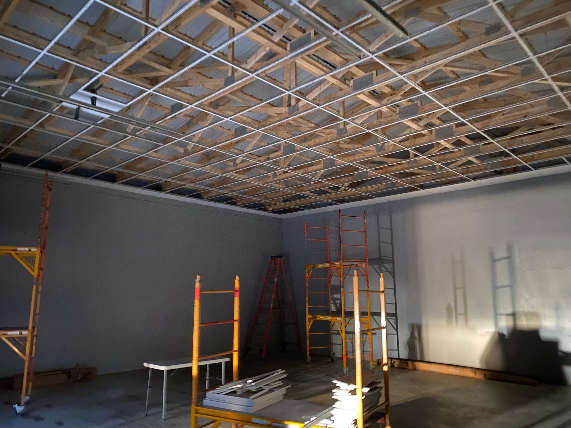 Construction site interior. Wooden ceiling frame with metal grid, gray walls, and scaffolding.