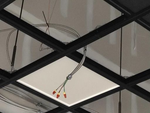 Black grid ceiling with a white tile; wires hang down.