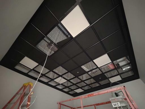 Black grid ceiling with lights and exposed wiring; a ladder and a scaffold are in the foreground.